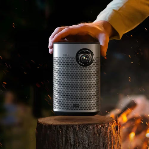 Xgimi projector on a wooden stump with a person's hand holding it, against a dark background.